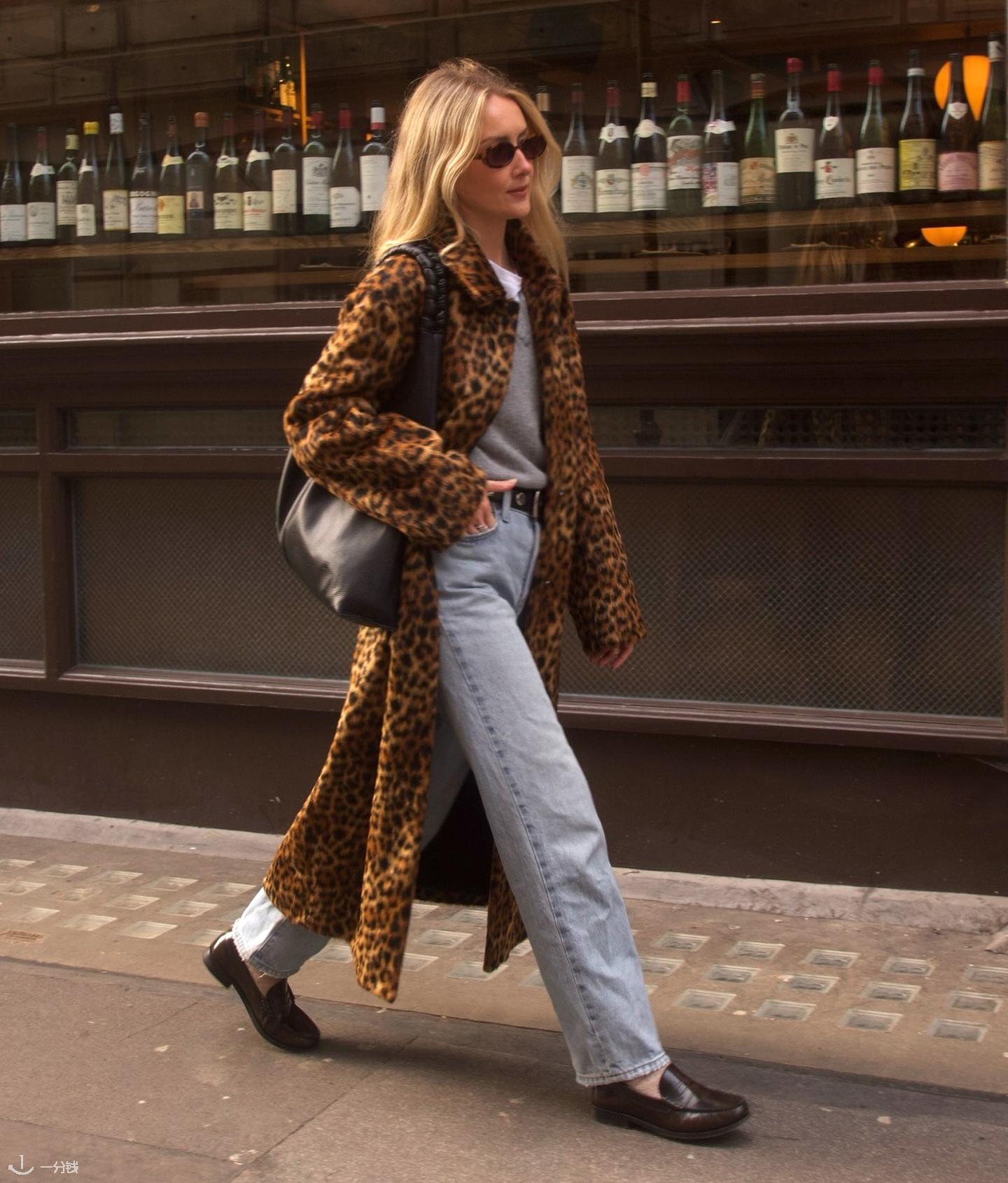 英国时尚博主 Chloe Kath Butler 身穿豹纹外套，内搭白色T恤，外穿灰色V领毛衣，腰系黑色铆钉腰带，手提黑色托特包，下身穿着浅色牛仔裤和棕色乐福鞋，走在伦敦街头。